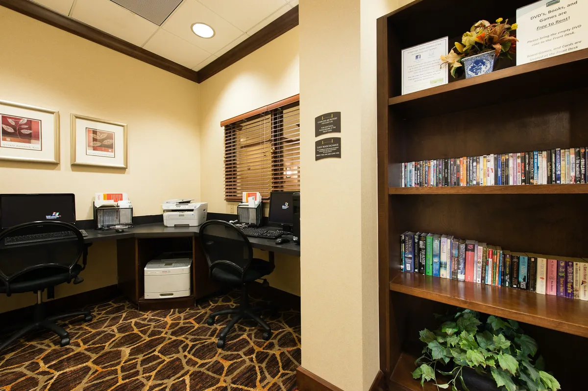 Featuring computers, a printer, a bookshelf, decorative plants, and framed art, this image shows a functional business center ideal for productivity. The environment appears quiet and organized, with spaces for working, reading, or completing projects.