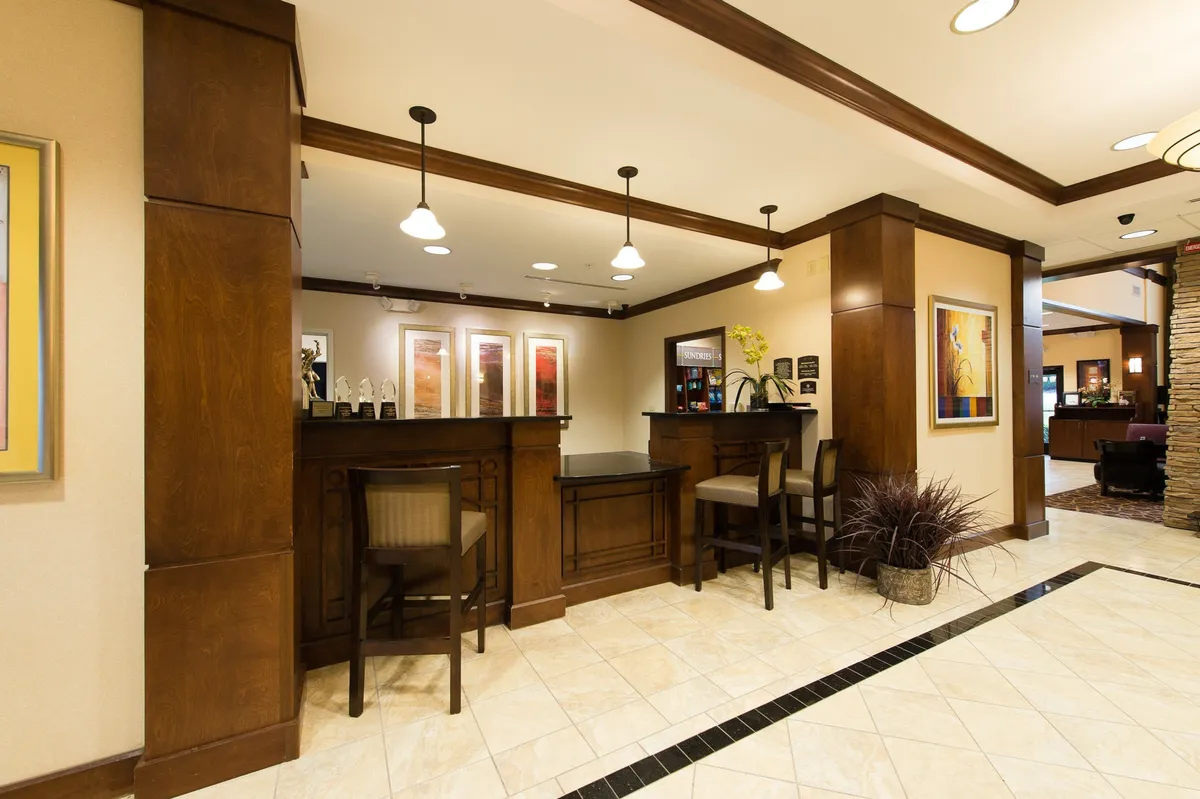 This image captures the reception area with a welcoming front desk, decorative artwork, and a comfortable seating zone. The scene suggests guests checking in and engaging in casual interactions, all under warm lighting that sets a professional yet inviting tone.