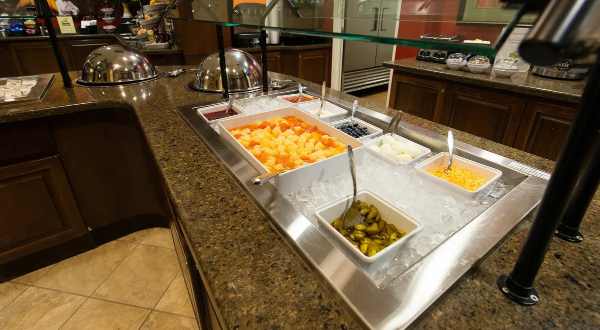 This interior breakfast scene highlights a vibrant self-service toppings bar with fresh fruit salad and condiments. The cheerful setting is perfect for family gatherings, suggesting a bright start to the day before exploring local attractions.