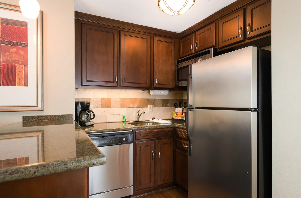 A spacious, fully equipped kitchen featuring dark wooden cabinets, stainless steel appliances such as a stove, microwave, and full-size refrigerator, as well as a granite countertop. Colorful artwork adds a touch of warmth and vibrancy to the space, making it ideal for cooking and family gatherings.