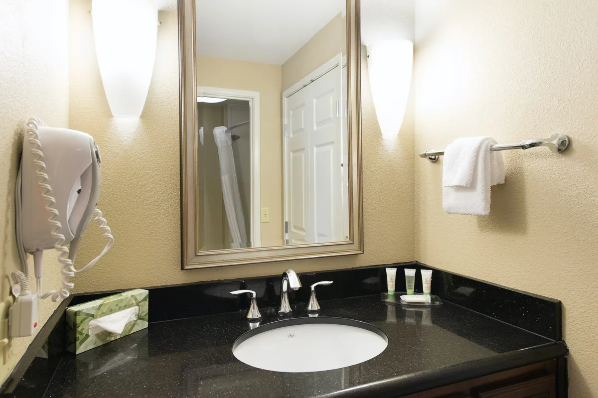 A modern, well-lit bathroom with a stylish mirror, ample sink space, elegant lighting fixtures, and a neatly arranged towel rack. The clean and inviting atmosphere promotes a refreshing experience, ideal for personal care routines.