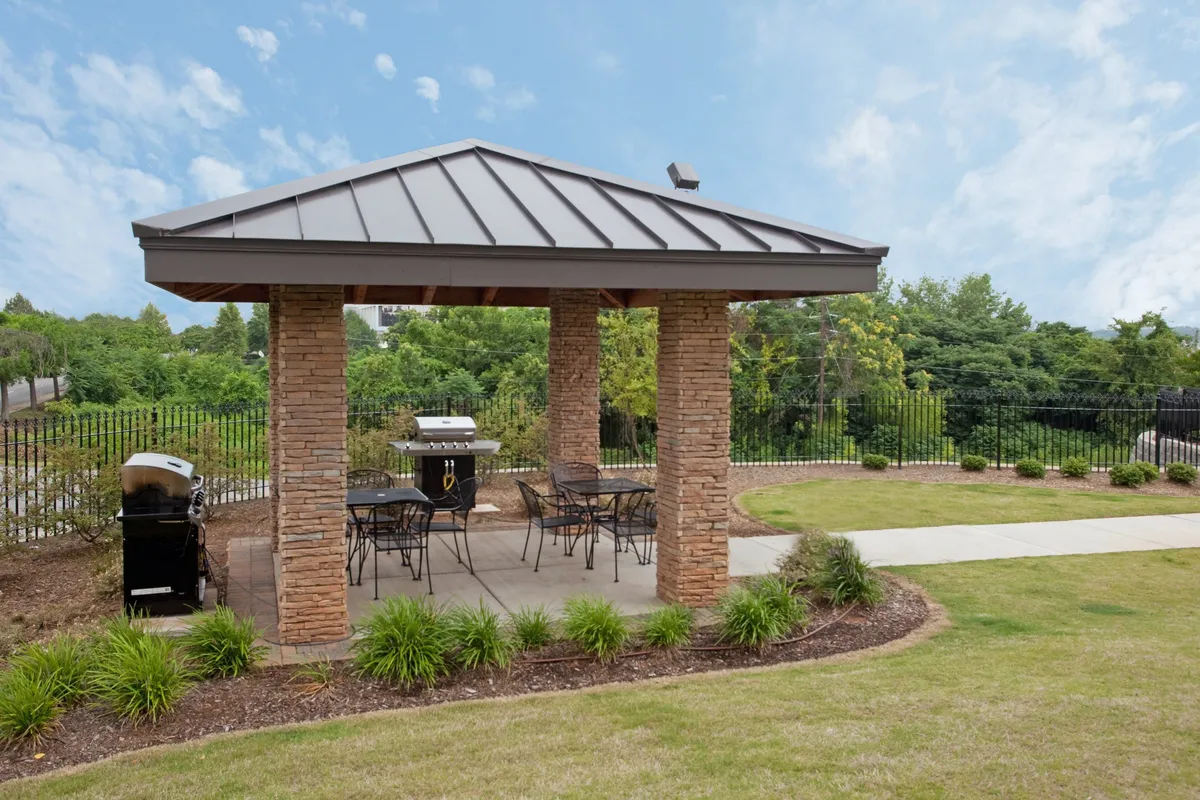 An outdoor area featuring a charming gazebo, grill, and plenty of seating, set amid lush landscaping. The space is designed for barbecuing, socializing, and enjoying the outdoors, ideal for family picnics or small gatherings.